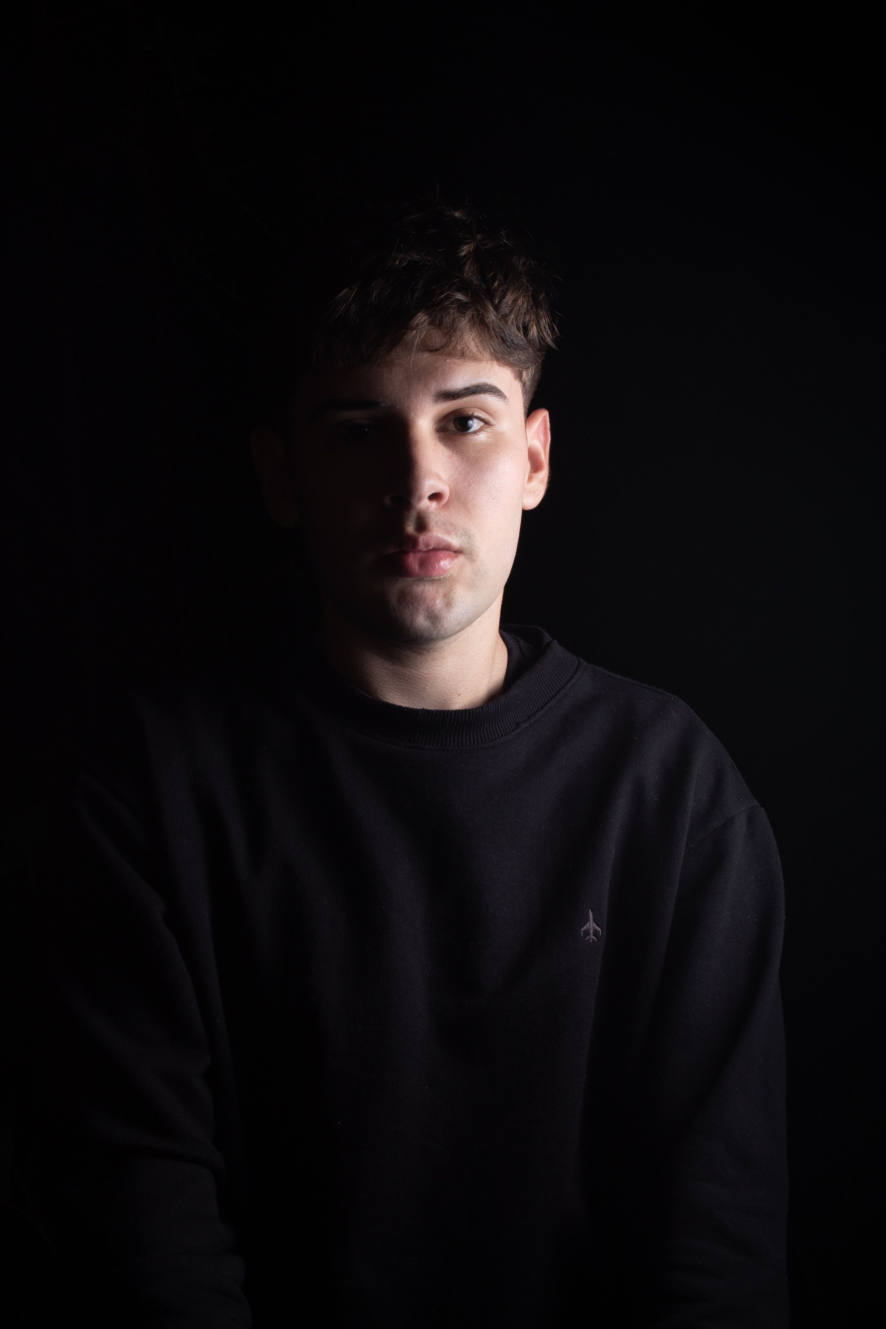 Free Emotive studio portrait of a young man in a black pullover against a dark background. Stock Photo