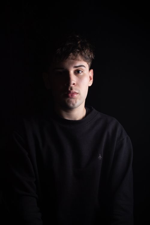 Free Emotive studio portrait of a young man in a black pullover against a dark background. Stock Photo