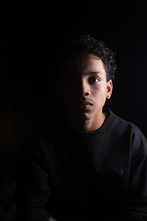 Free Dramatic portrait of a young man with curly hair in a low-light studio setting, highlighting fashion and mood. Stock Photo