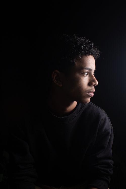 Free A dramatic side-lit portrait of a young man looking contemplatively into the light against a dark background. Stock Photo