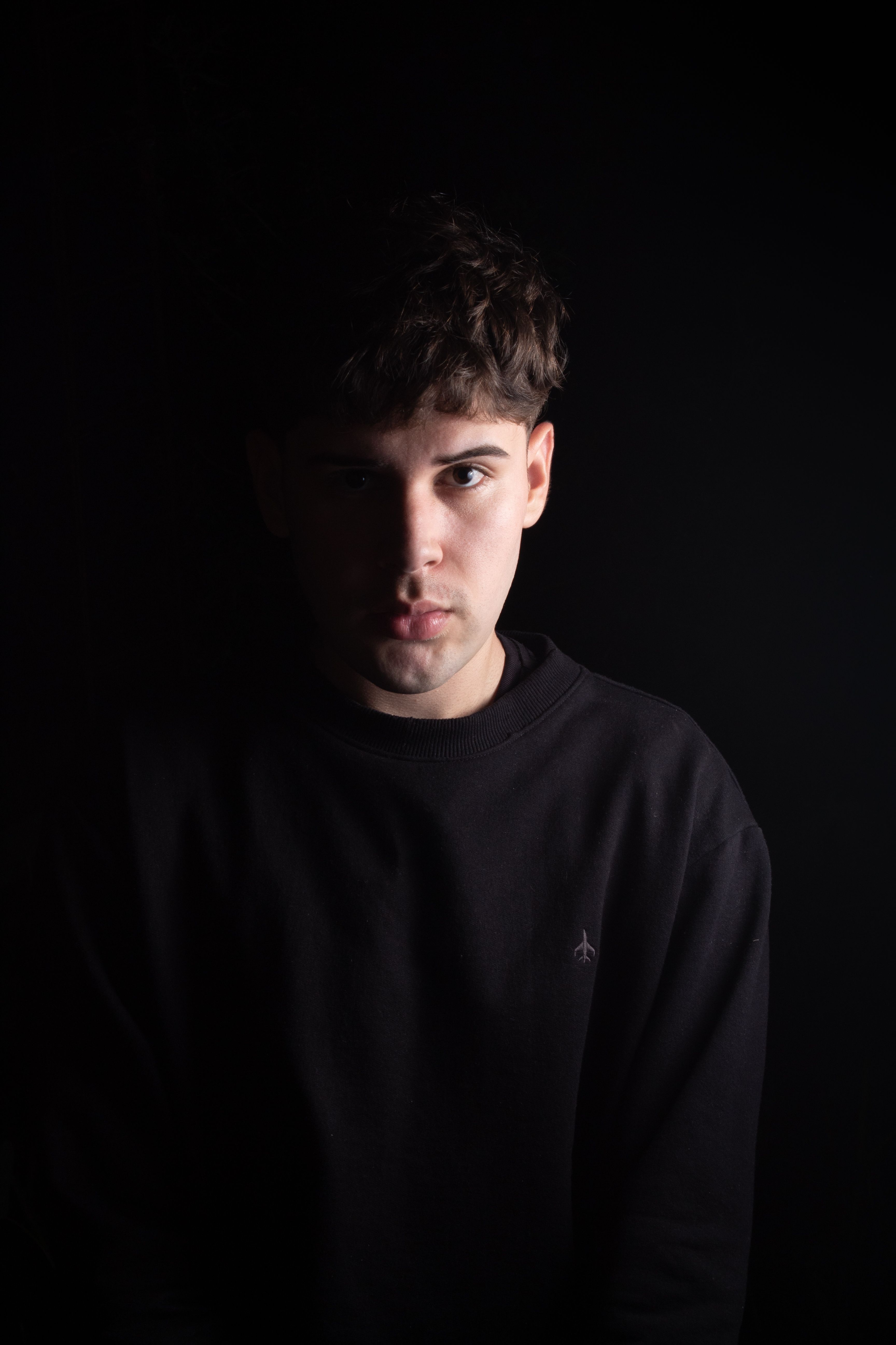 Free Artistic portrait of a man in a black sweater against a dark background, highlighting dramatic lighting. Stock Photo