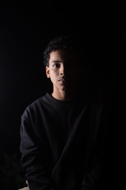 Free A dramatic studio portrait of a man in a black pullover against a dark background. Stock Photo