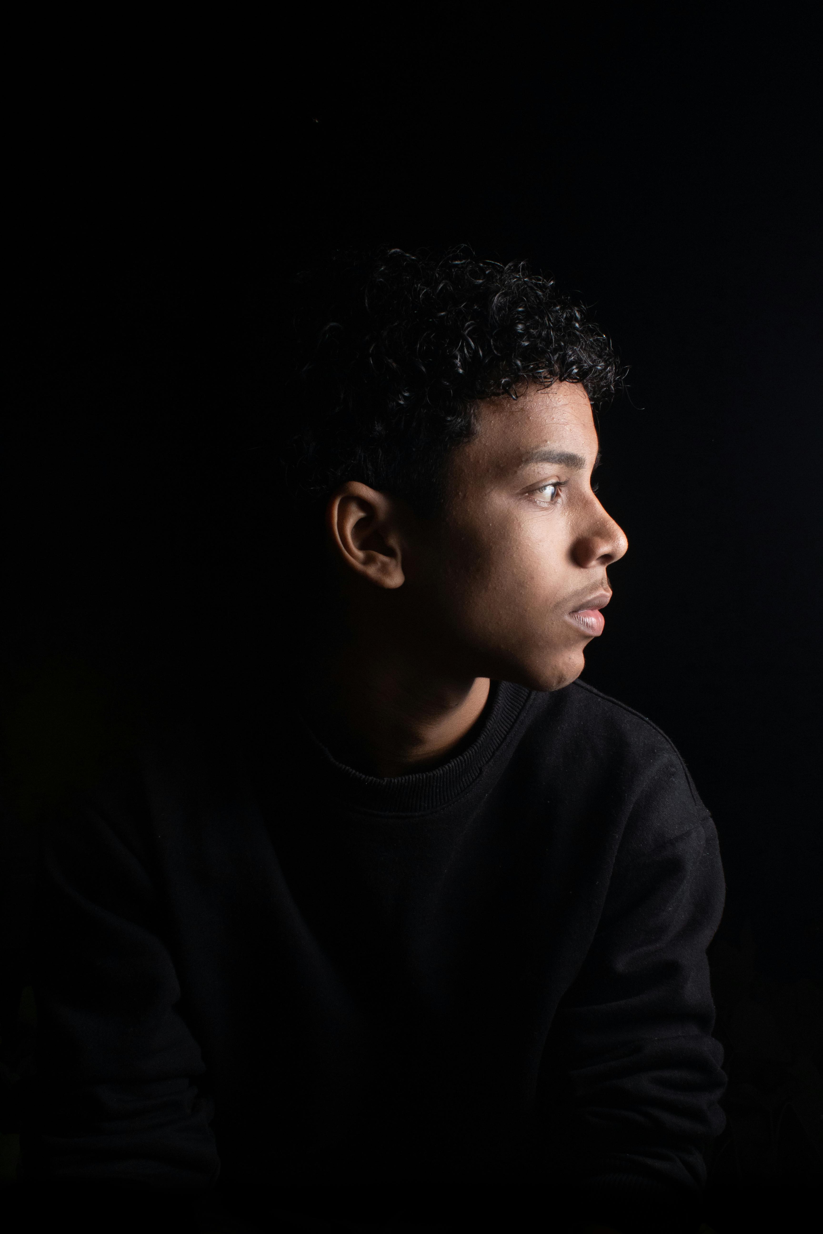 Dramatic portrait of a young man against a dark background, highlighting his thoughtful expression.
