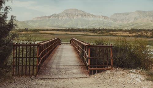 A wooden bridge over a river with mountains in the background
