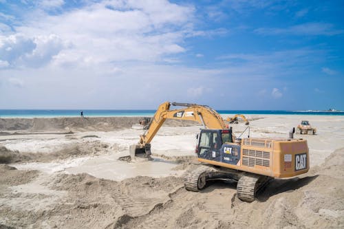 An excavator and a construction worker at a beach site, engaging in land preparation for development.