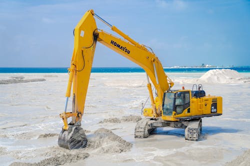 A Komatsu excavator working on a beach construction site, moving sand for land reclamation.