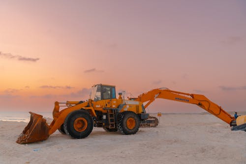 A large orange construction vehicle on the beach at sunset