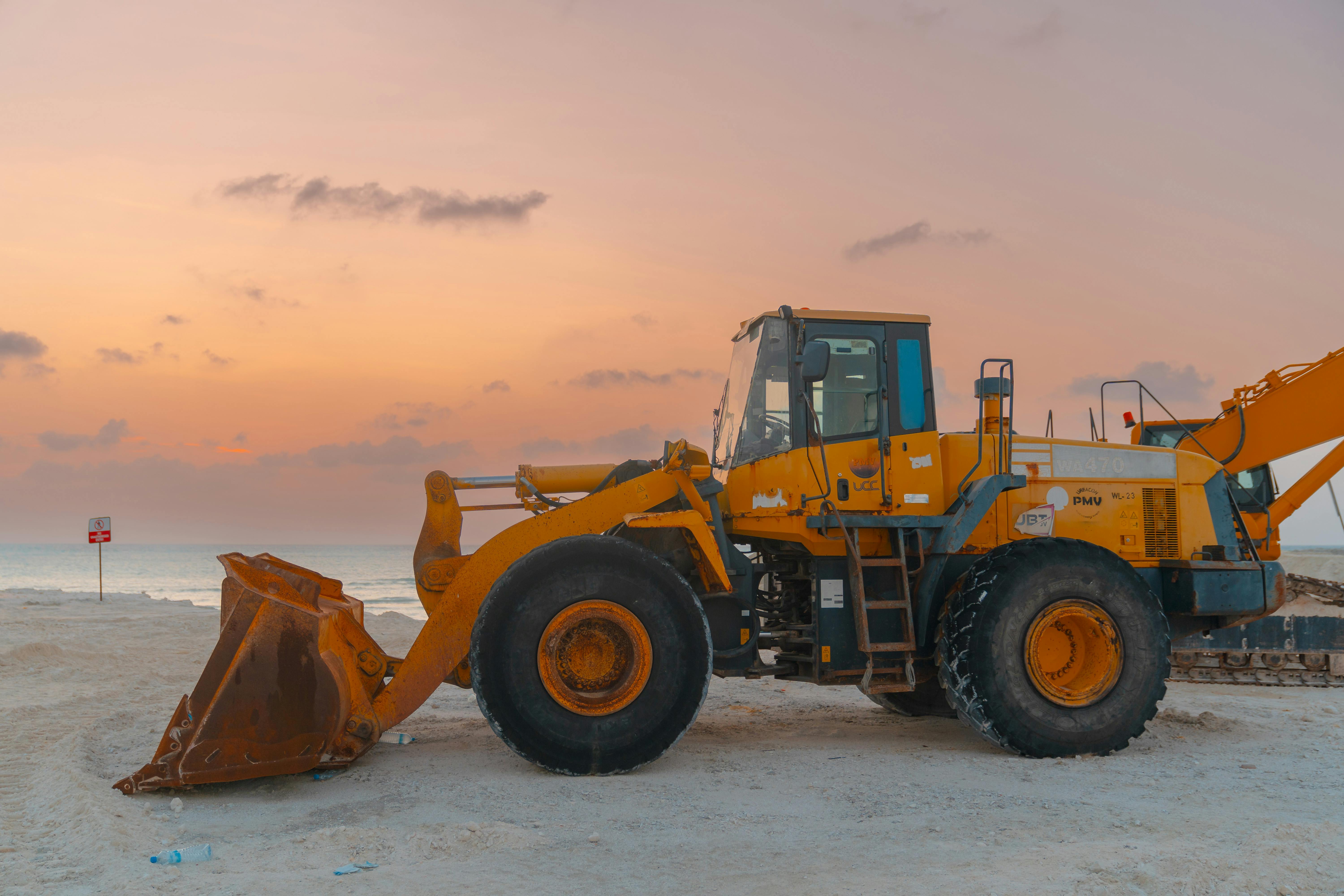 A bulldozer on a beach during sunset, ideal for projects involving coastal construction.