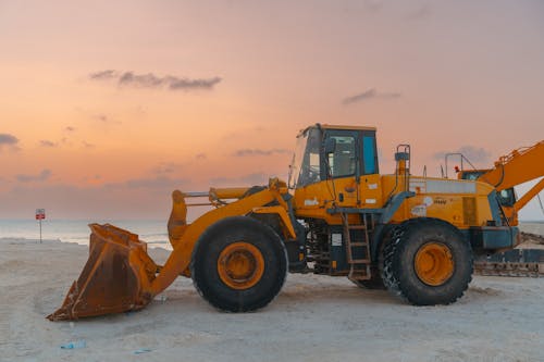 A close-up of a yellow bulldozer on a sandy beach at sunset, showcasing construction machinery.  Close-up of a yellow bulldozer on a sandy beach at sunset.