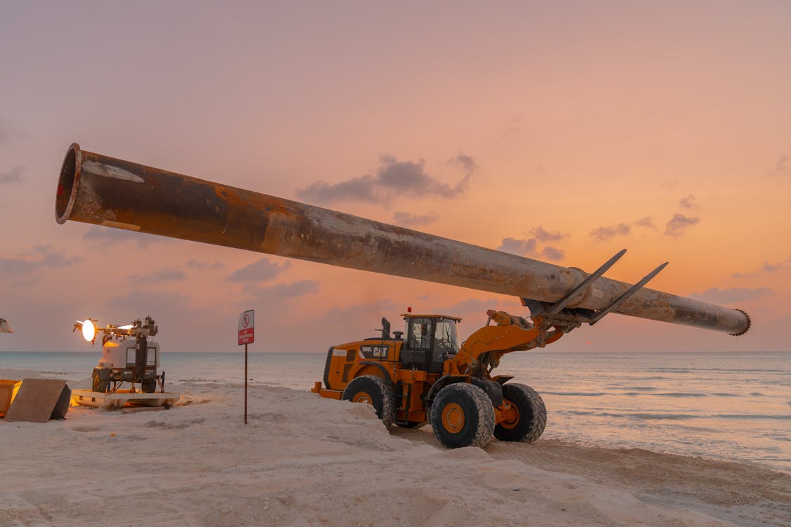 A large pipe is being pulled by a tractor on the beach