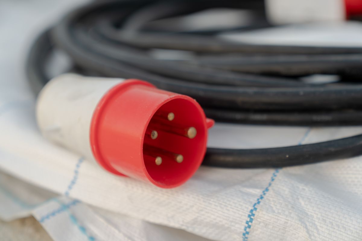 Close-up of a red industrial electrical cable plug on a construction site, part of a temporary power distribution set-up