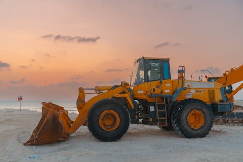 A bulldozer at a beach construction site during sunset, ready for the next day's work.  Yellow bulldozer at a beach construction site during sunset with a beautiful orange sky.