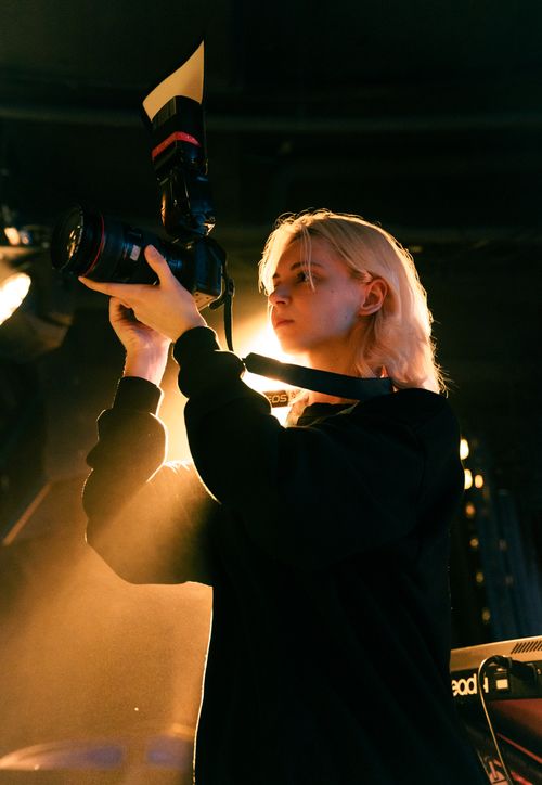 Free Blonde female photographer capturing images under dramatic studio lighting with a professional camera. Stock Photo