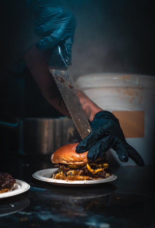 Hands in Gloves Cutting Burger on Plate