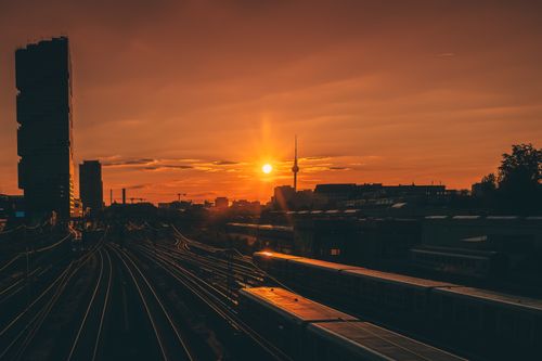 Free Dramatic Berlin cityscape at sunset with TV Tower silhouette, railway tracks, and orange sky. Stock Photo