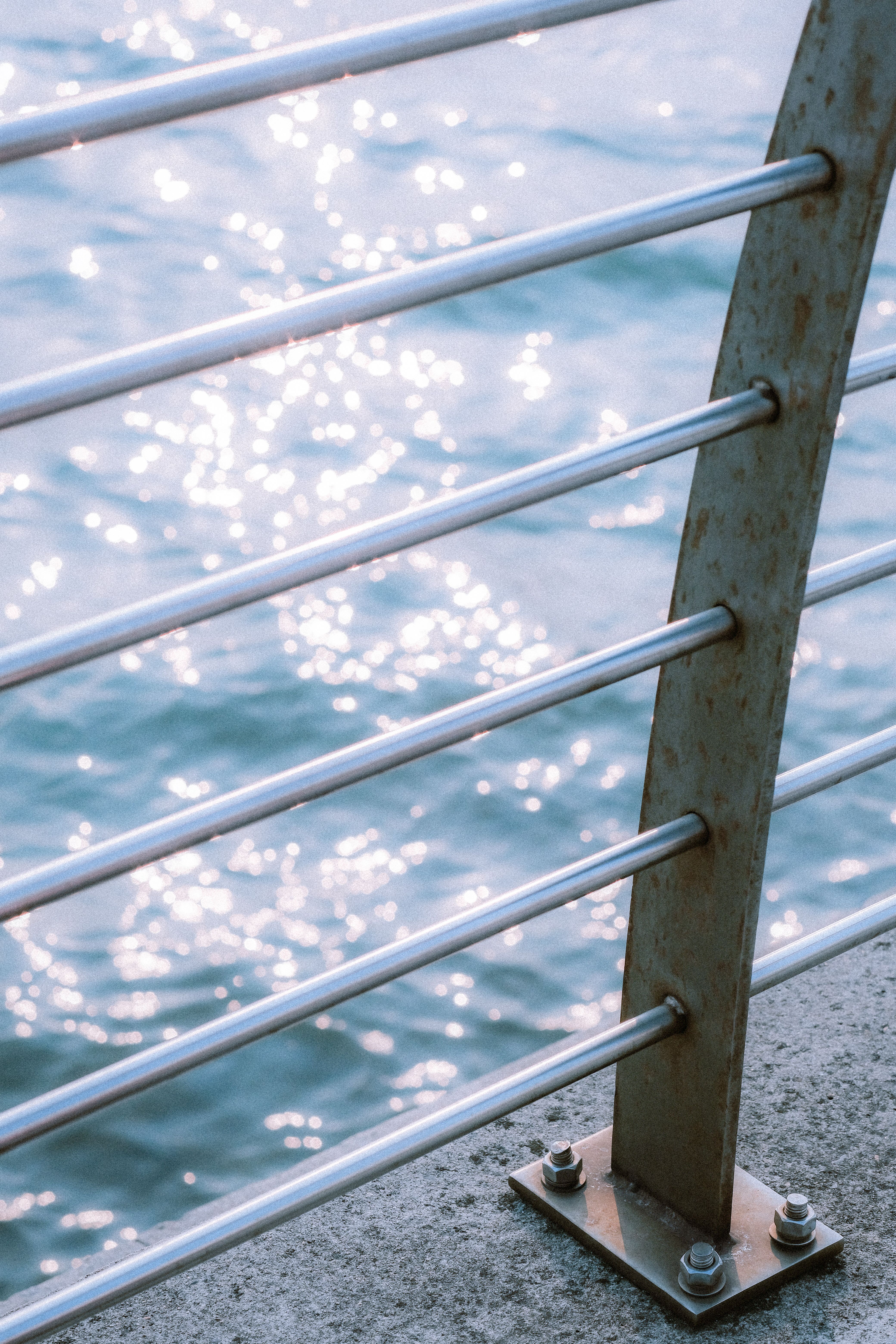 Close-up of a metal railing with sparkling sea reflections in the background.