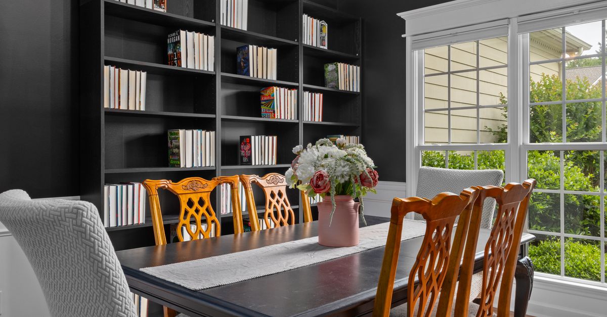Luxurious dining room featuring bookshelves, elegant chairs, and a vase of flowers by the window.