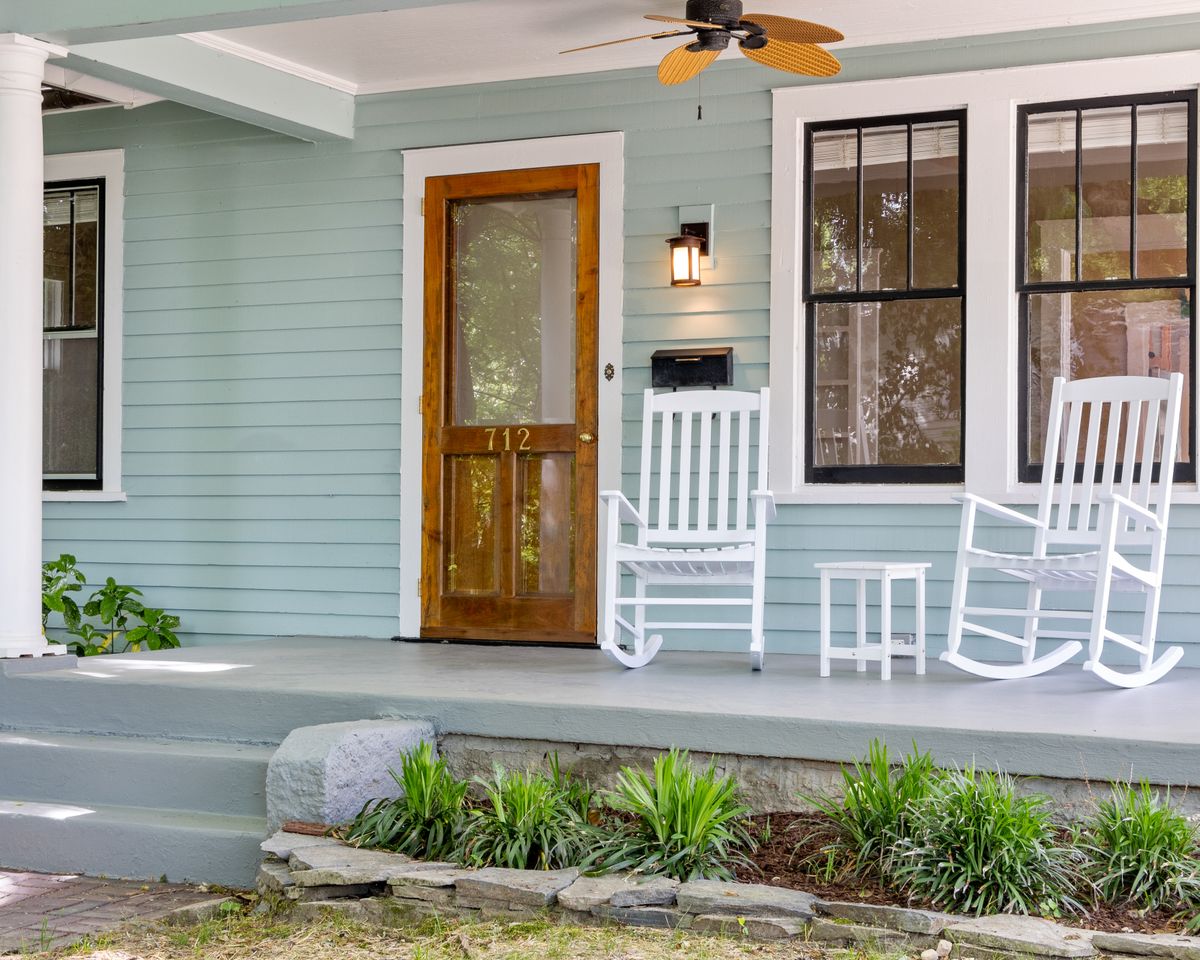 Inviting front porch featuring white rocking chairs and a wooden door.
