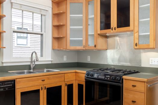 Bright modern kitchen featuring wooden cabinets, oven, and stainless steel sink.