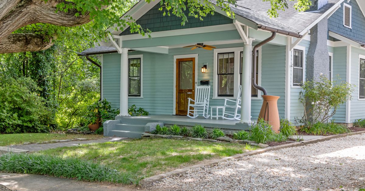 Quaint suburban home with a cozy porch and rocking chairs, surrounded by lush greenery.