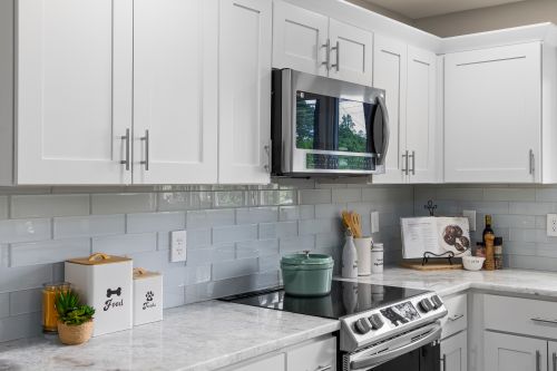 Free Bright modern kitchen featuring white cabinets, marble countertops, and stainless steel appliances. Stock Photo