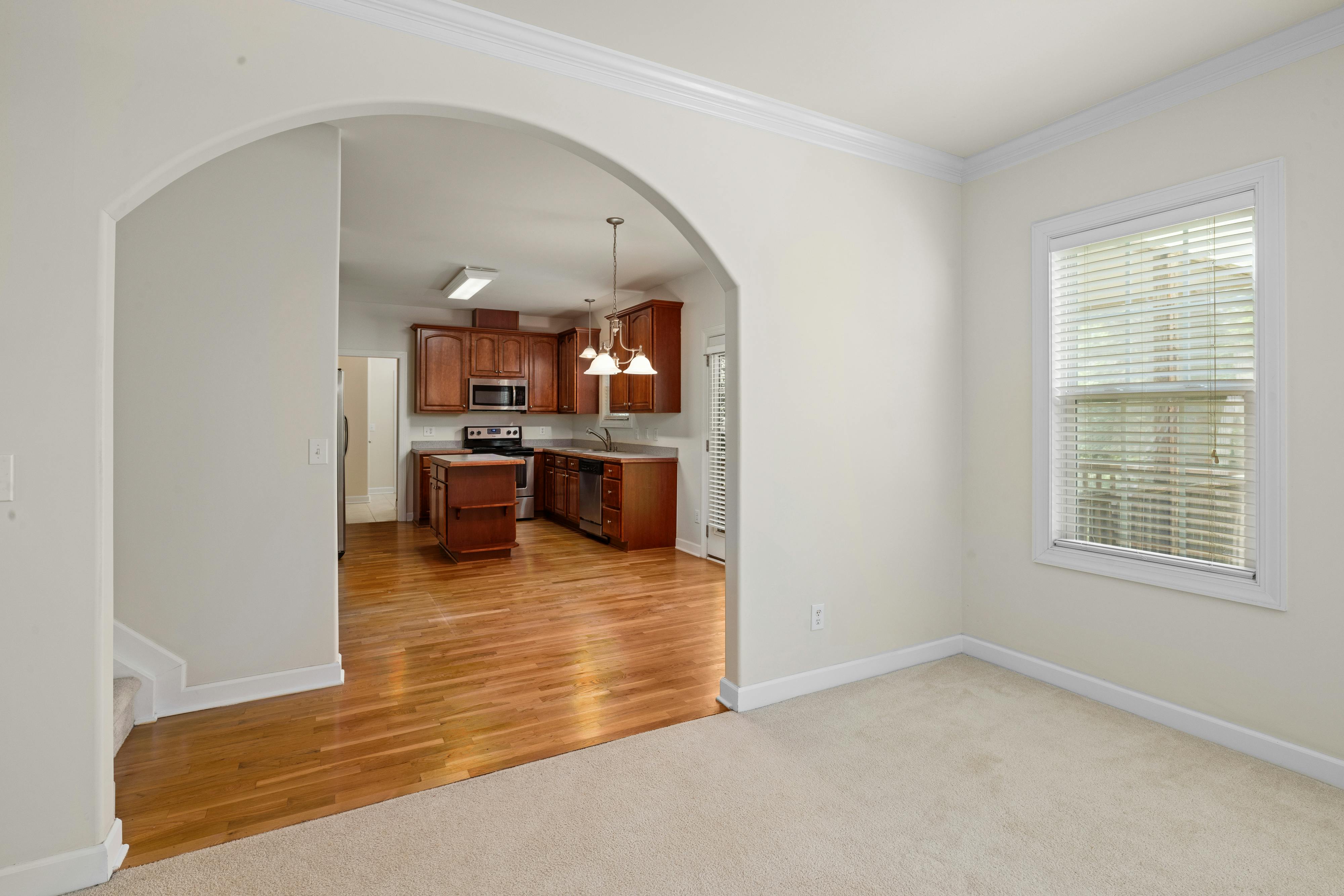 Spacious kitchen with wooden cabinets and archway leading to bright living area.