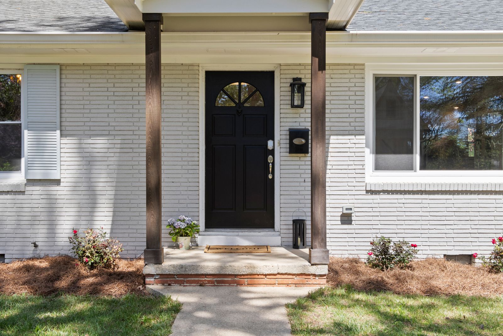 Close-up of a white brick home's covered entry with a black front door, arched window, and flanking flowerbeds, Brush Hill, Naperville IL