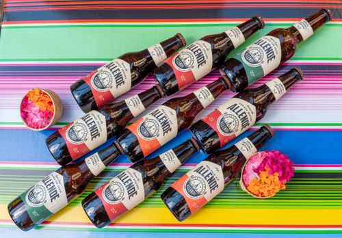 Free Top view of Mexican beer bottles with colorful labels on a vibrant striped tablecloth, photographed in CDMX. Stock Photo