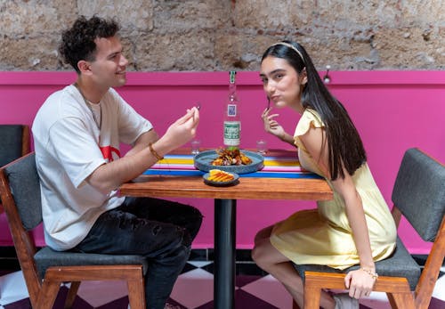 Free A man and woman sitting at a table with a pink wall behind them Stock Photo