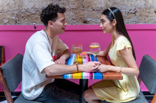 Free Young couple holding hands while enjoying drinks at a vibrant CDMX restaurant. Stock Photo