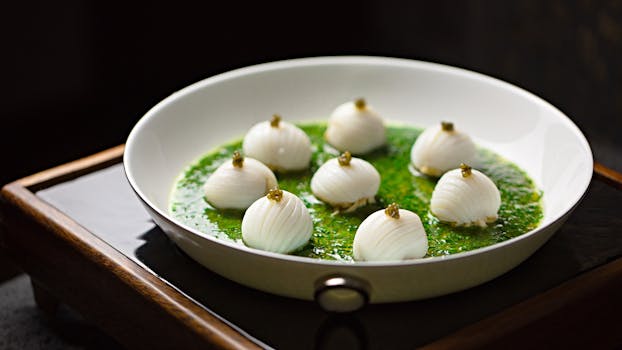 A gourmet dish beautifully presented in a white bowl, featuring white layered spheres on a bed of vibrant green sauce.