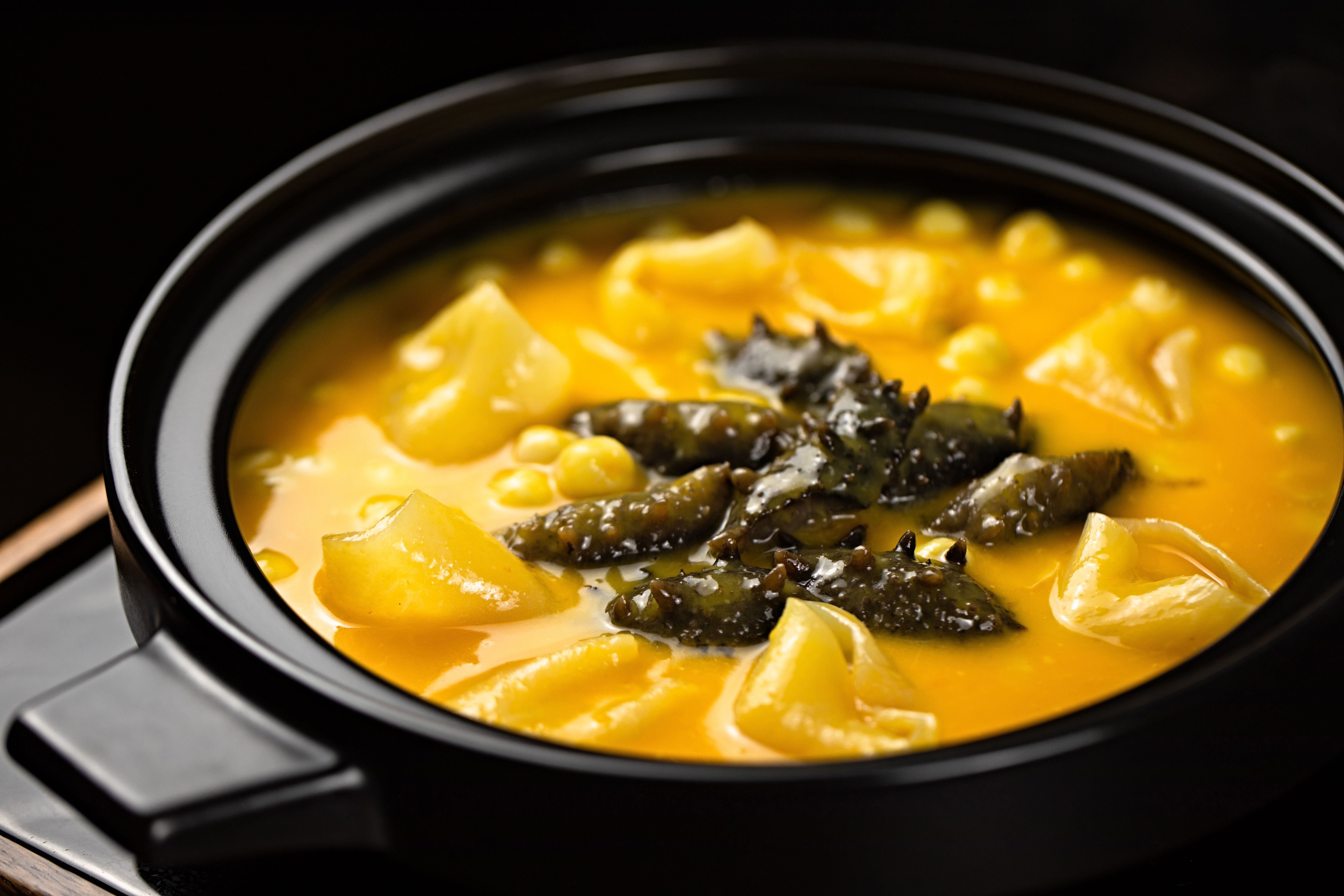 Close-up of a savory yellow stew featuring sea cucumber and dumplings in a black pot.