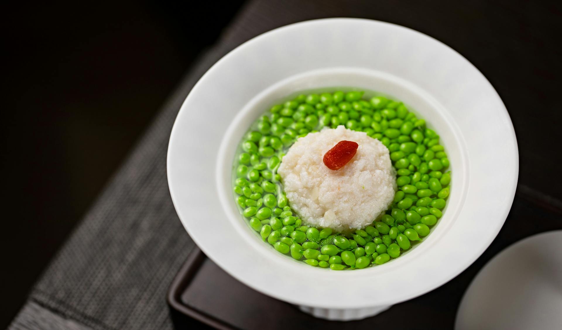 Asian dish showcasing a white meatball on green peas, contrasting colors.