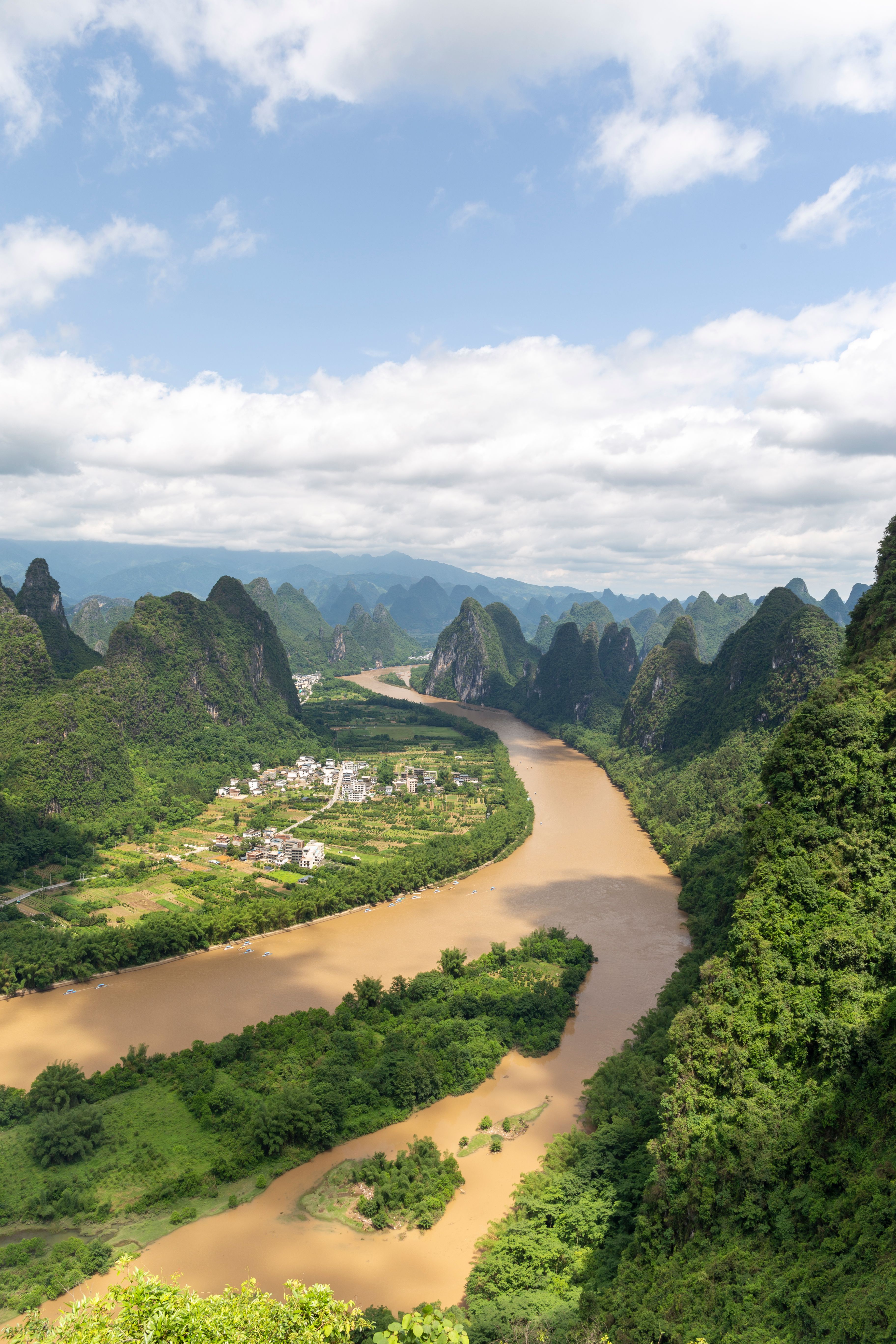 Breathtaking aerial view of Li River meandering through lush karst mountains under a partly cloudy sky in Guilin, China.