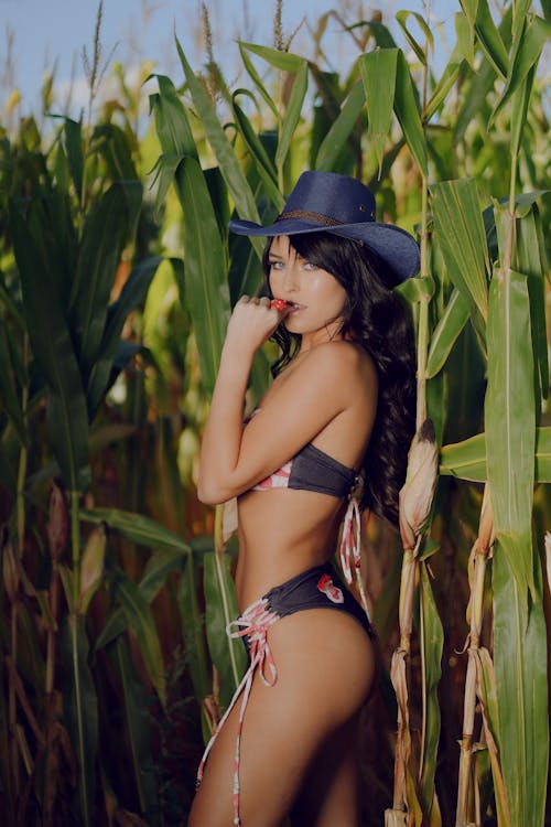 A woman in a hat and bikini standing in a corn field