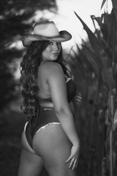 A woman in a bikini and cowboy hat posing in front of a corn field