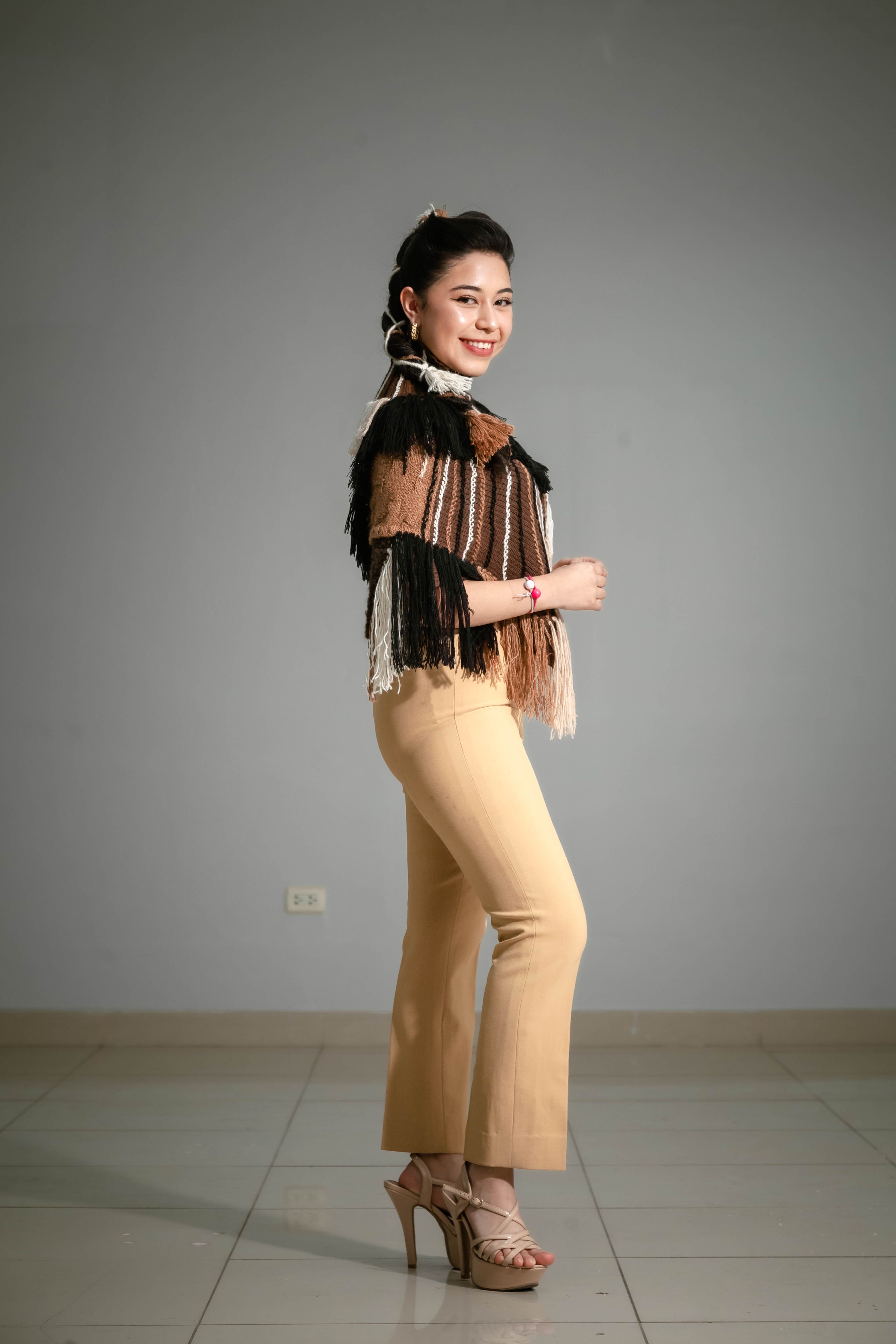 Confident woman posing indoors in a tasseled top and beige pants with a bright smile.
