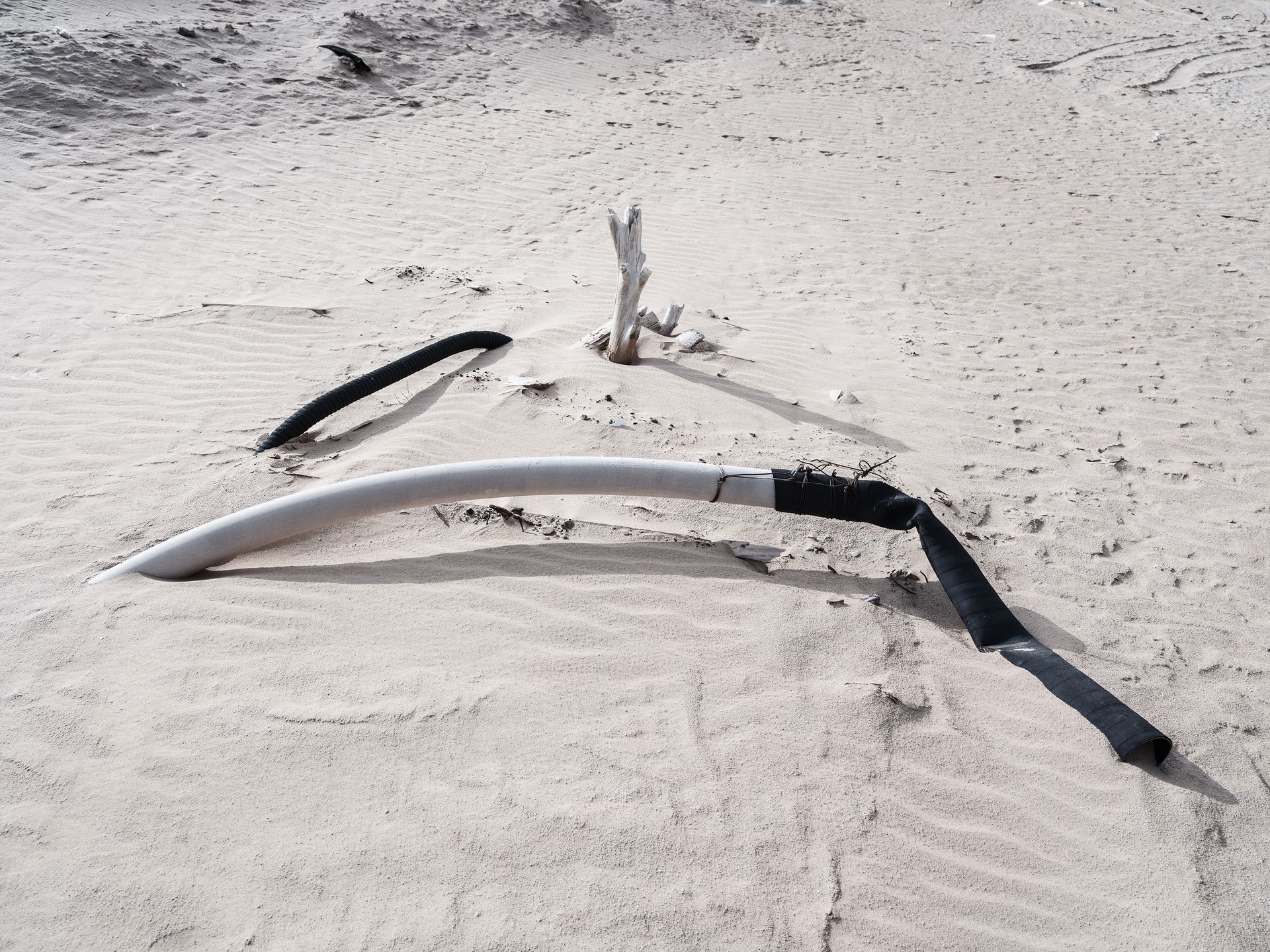 A broken pipe and driftwood on a sandy beach, symbolizing pollution and environmental neglect.