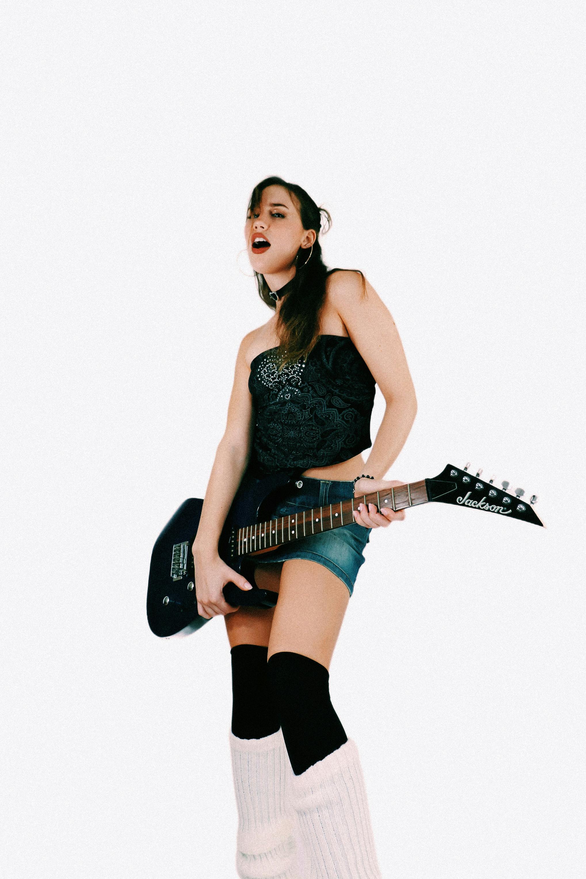Stylish young woman playing electric guitar with energy on a white background.
