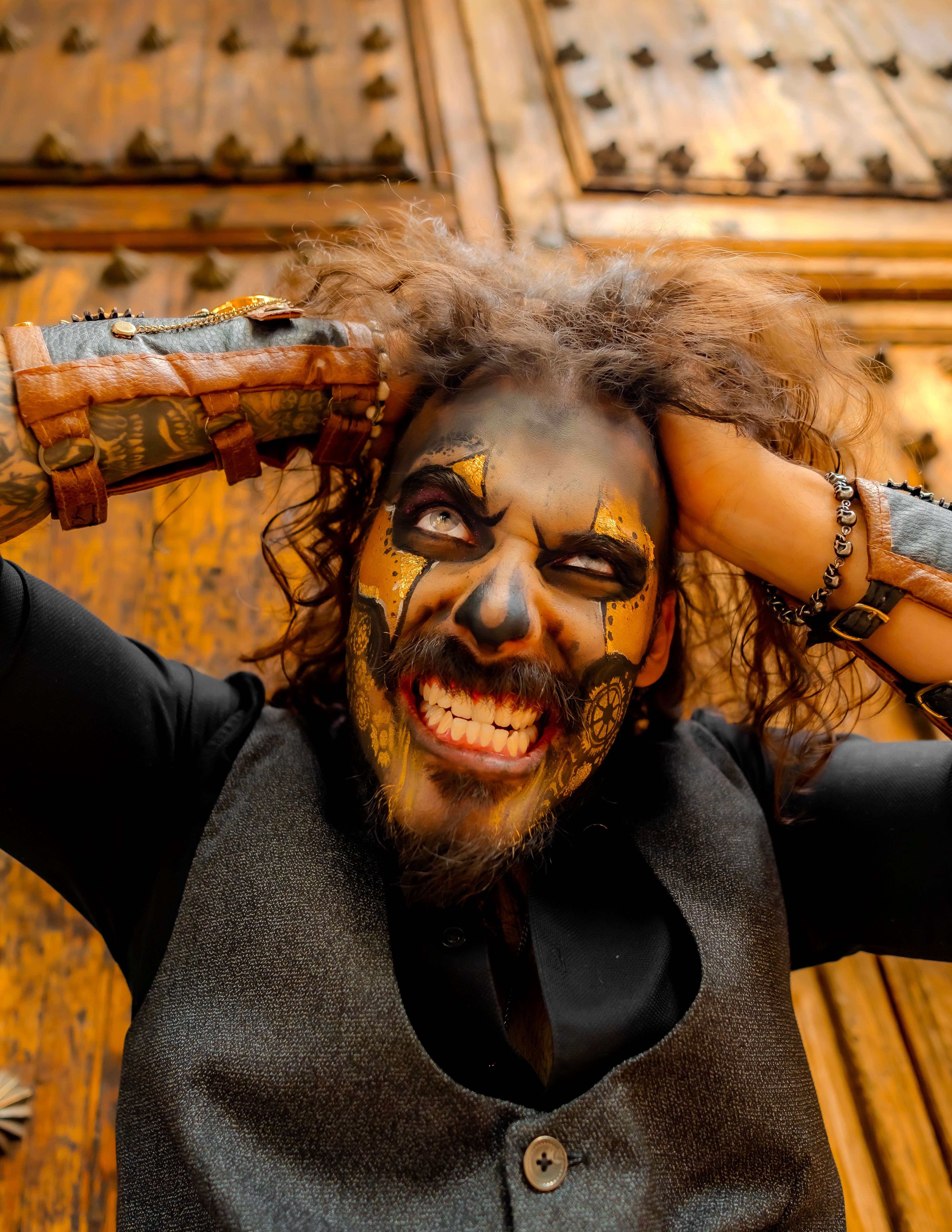 Dramatic portrait of a man with painted face and messy hair, expressing intense emotion against ornate wooden doors.