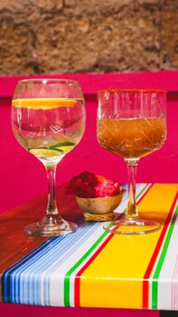 Two elegant cocktails on a vibrant, striped table with a pink backdrop, creating a festive atmosphere.