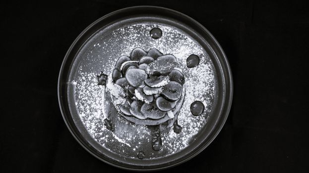 A monochrome view of a creatively styled dessert with fruit and powdered sugar on a plate.