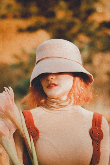 Woman in vintage fashion with a hat and flowers in an outdoor setting.
