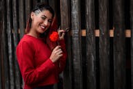 一位身穿红色毛衣的年轻女子手持玫瑰，在木栅栏旁微笑