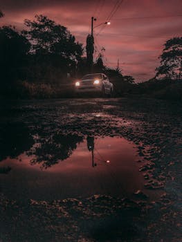 黄昏时，行驶在潮湿道路上的汽车，前灯在水坑中反射