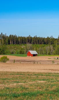 Charming red barn set amidst a sprawling rural landscape with clear blue skies and lush greenery.