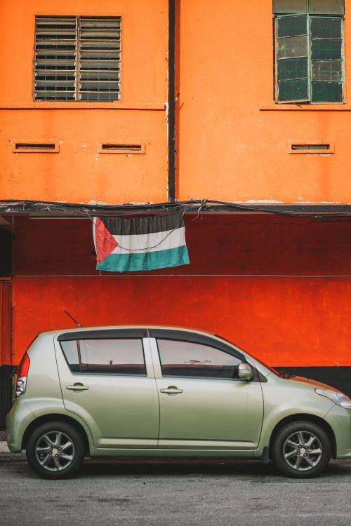 Free A green Perodua Myvi parked on an urban street with a flag backdrop in Klang, Malaysia. Stock Photo
