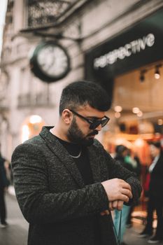 Stylish man with sunglasses checking time on watch in a bustling street of Baku, Azerbaijan.