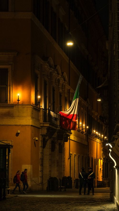 Free A vibrant Italian street scene with an illuminated building and flag at night. Stock Photo