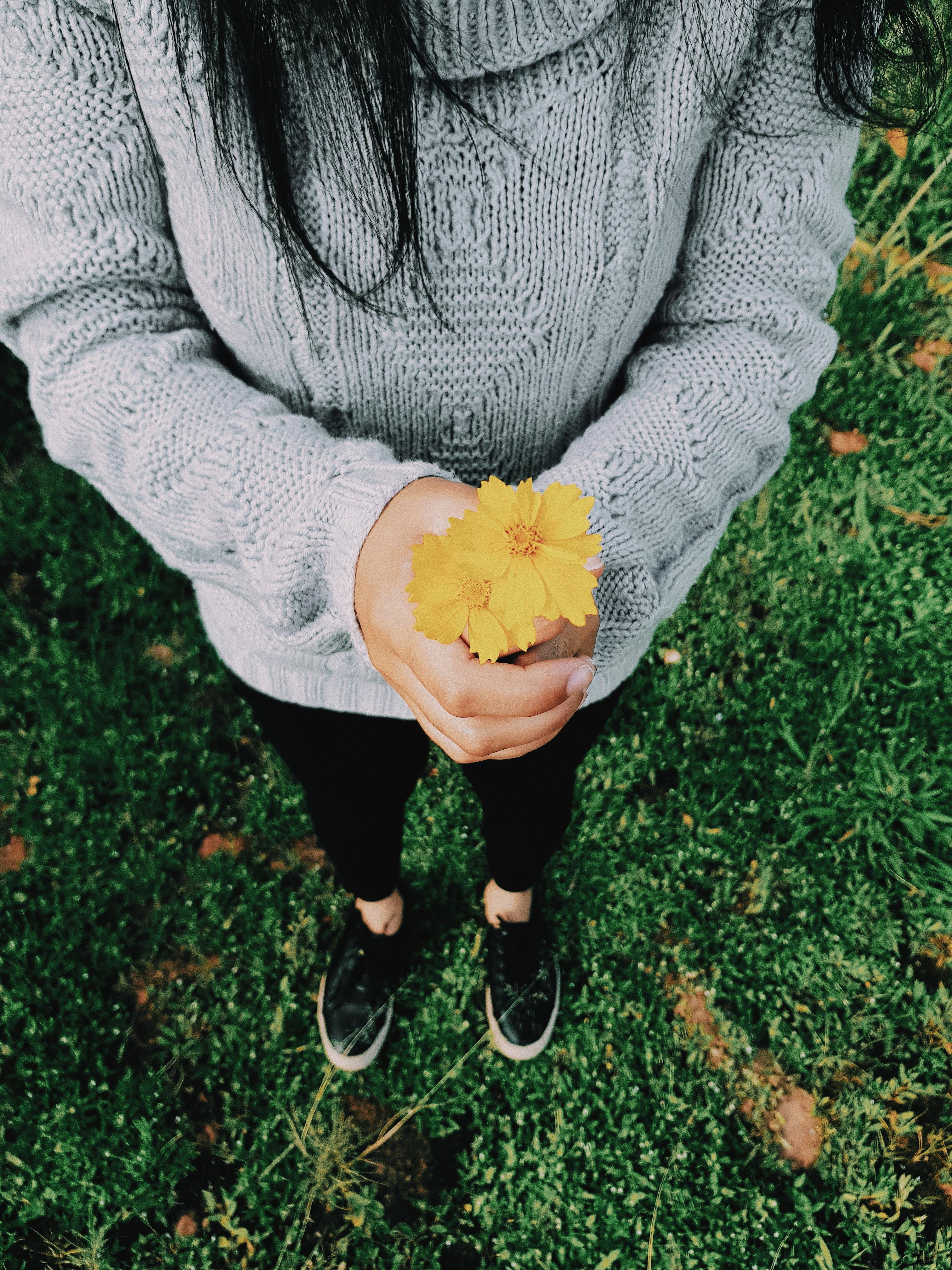 An overhead shot of a woman holding a yellow flower in a lush green field.